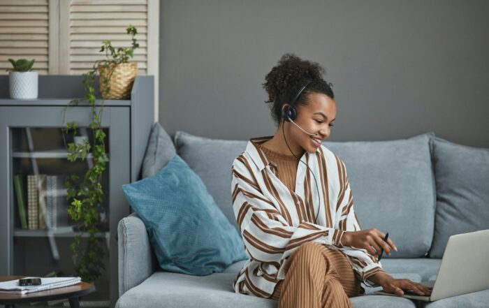 What Is A Virtual Assistant - Woman Sat On Sofa With Laptop Wearing Headset